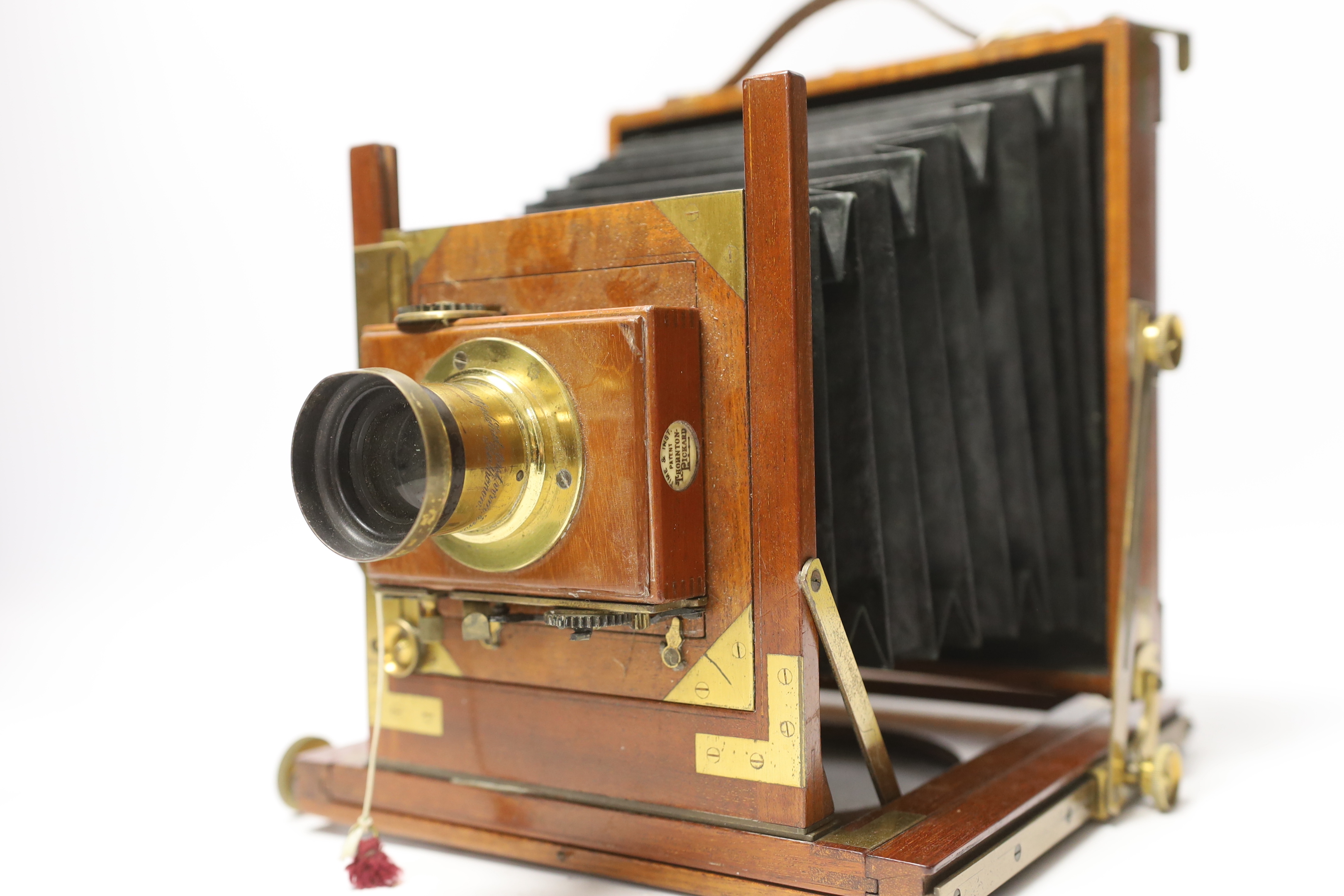 A late nineteenth century brass and mahogany half plate bellows camera with a lens and a shutter action by Thornton Pickard